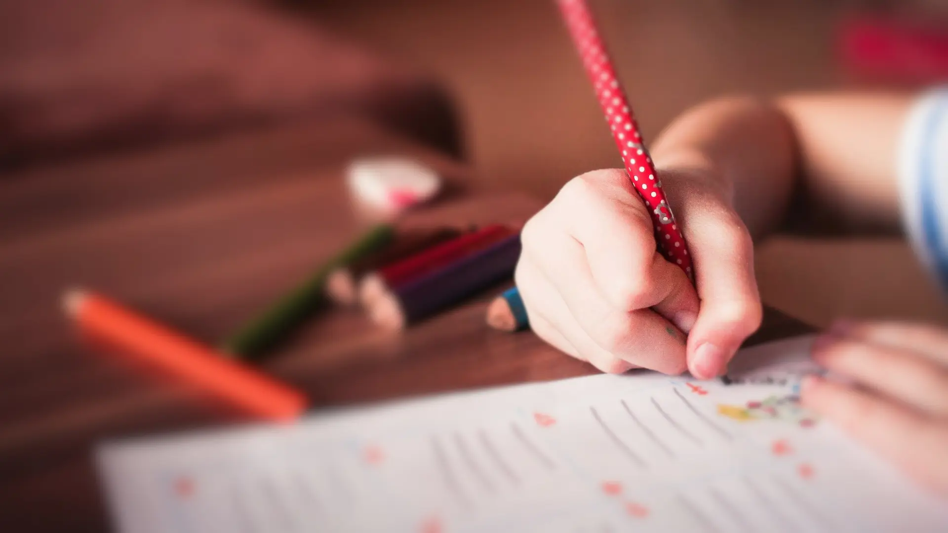 Photograph of a young girl's hand writing on a sheet of paper at a desk.