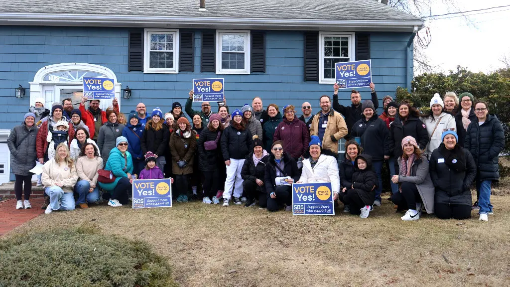 Group photo of canvassers in front of a blue house holding 'Vote Yes' signs