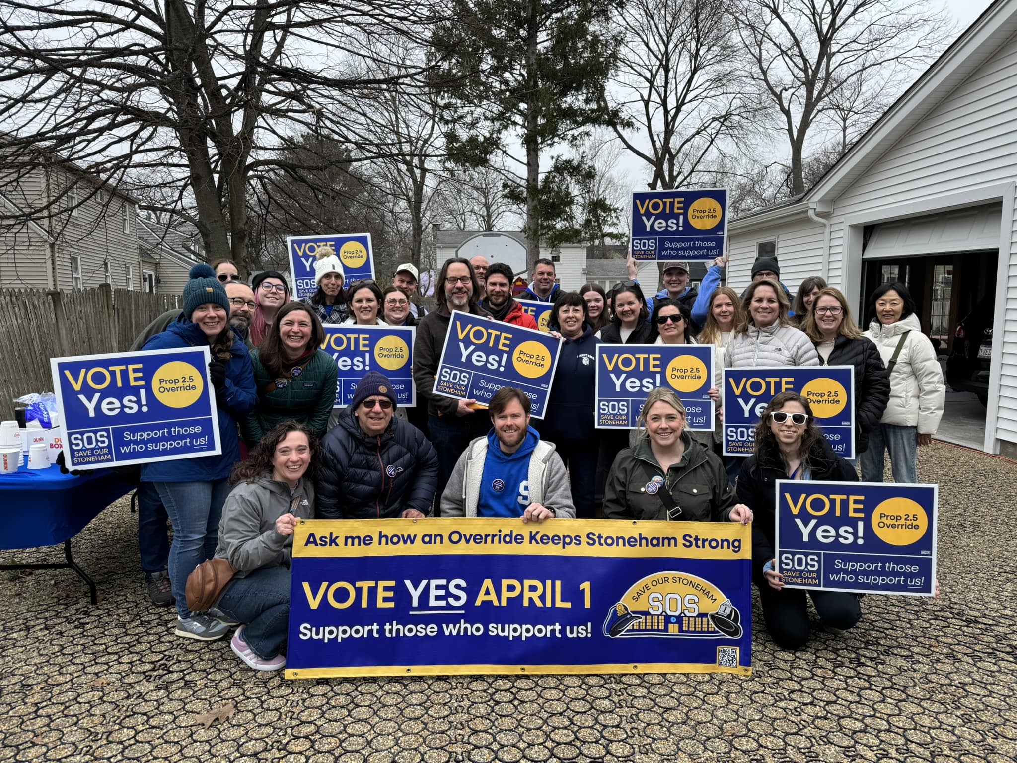 Group photo of canvassers in front of a white house holding 'Vote Yes' signs and banners